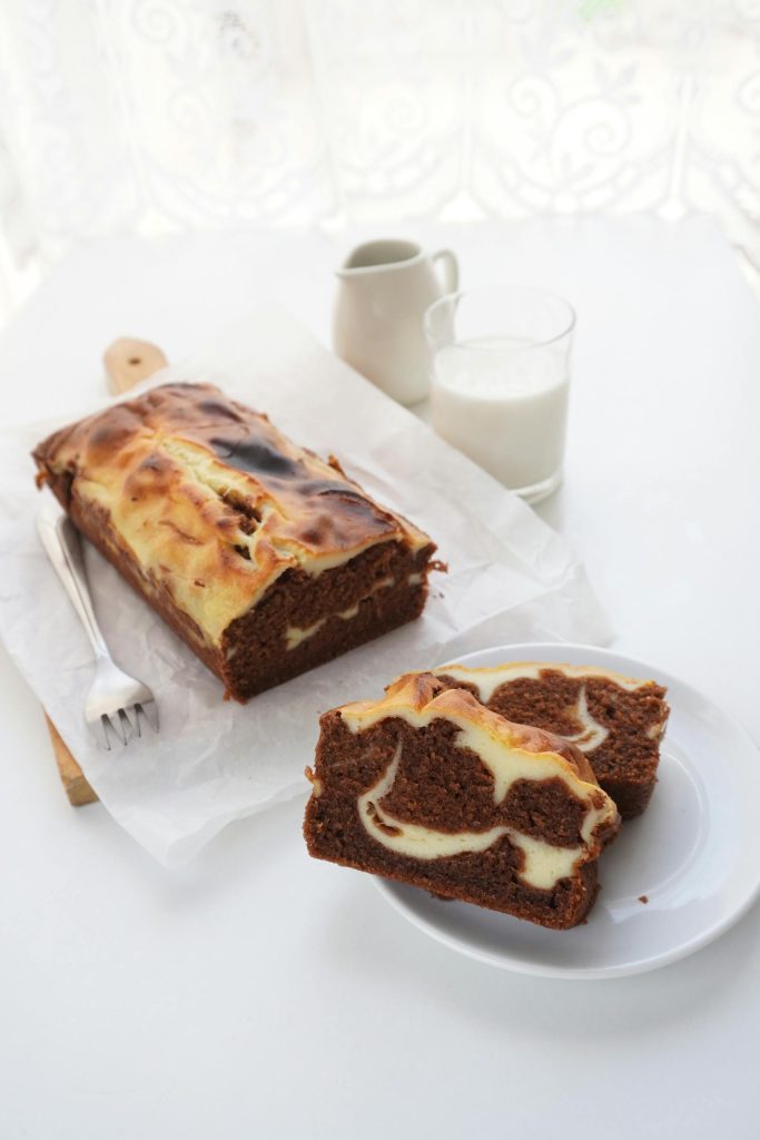 Delicious marble cake with cream cheese swirl on a white table with glass of milk.