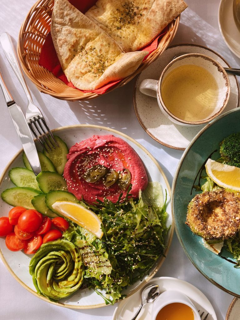 A vibrant vegan brunch featuring hummus, fresh veggies, tea, and pita bread on a sunlit table.