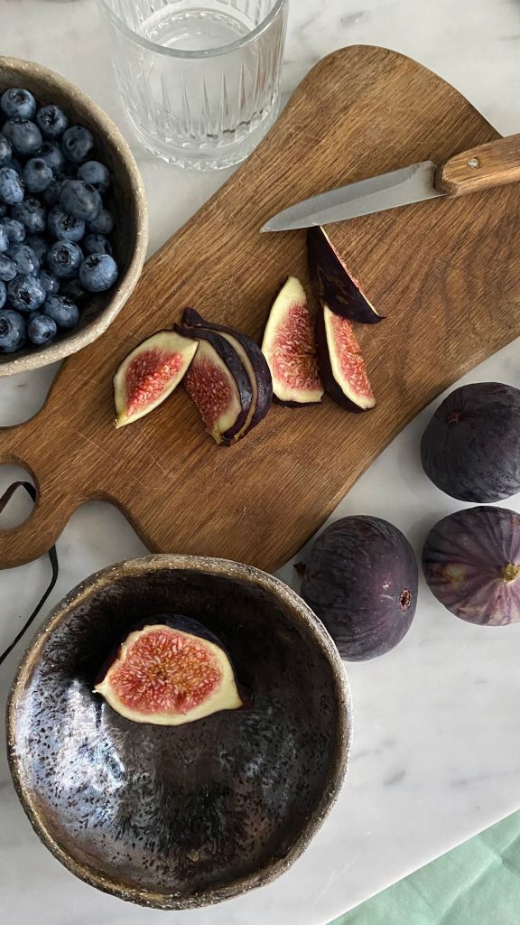 Aesthetic arrangement of sliced figs and blueberries on a wooden board with a knife.