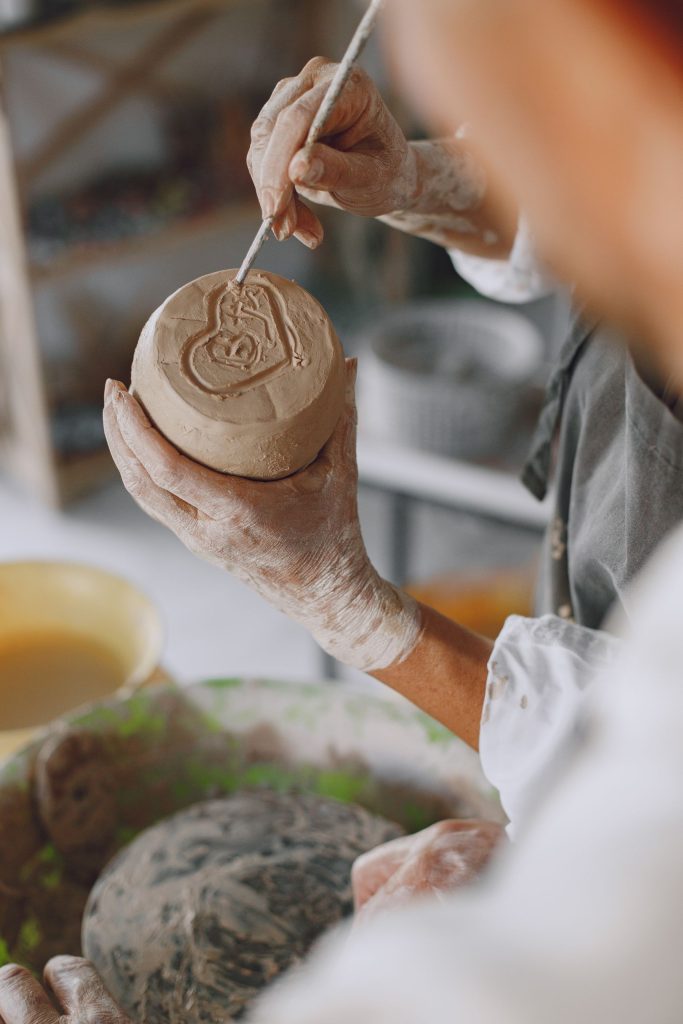 Close-up of hands crafting a clay pot, showcasing intricate detailing in pottery.