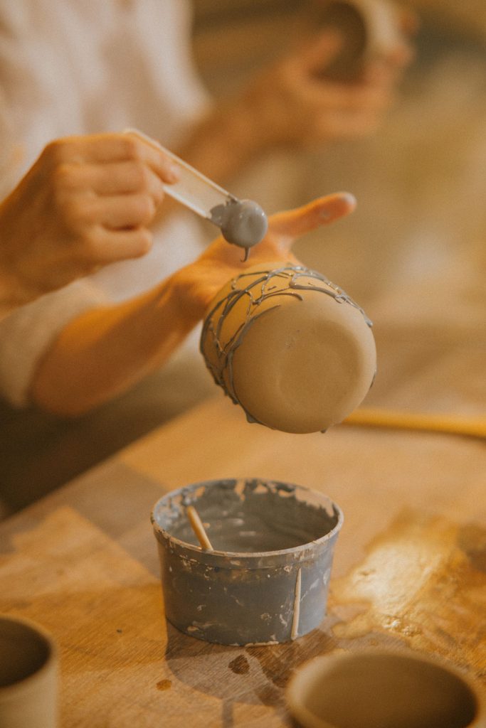 Close-up of hands molding and painting pottery in a creative workspace.