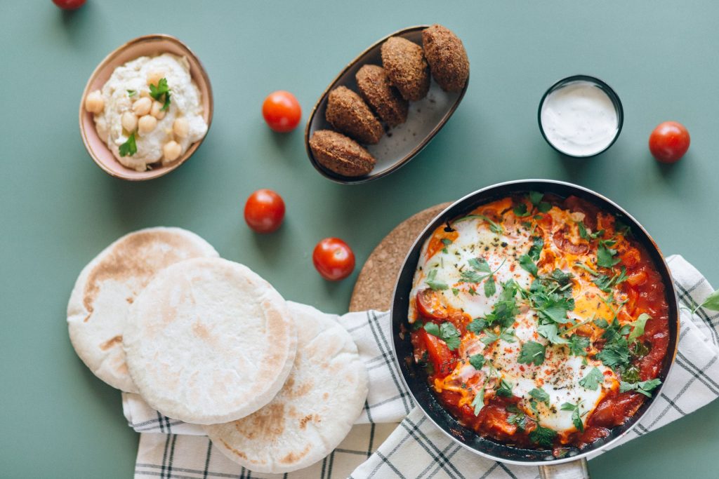 Delicious Middle Eastern breakfast with shakshuka, falafel, hummus, and pita bread on a table.