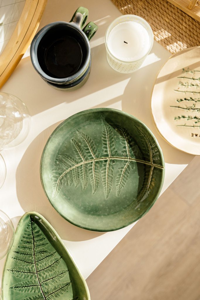 Top view of green ceramic plates with fern imprints on a sunlit table, creating a natural aesthetic.